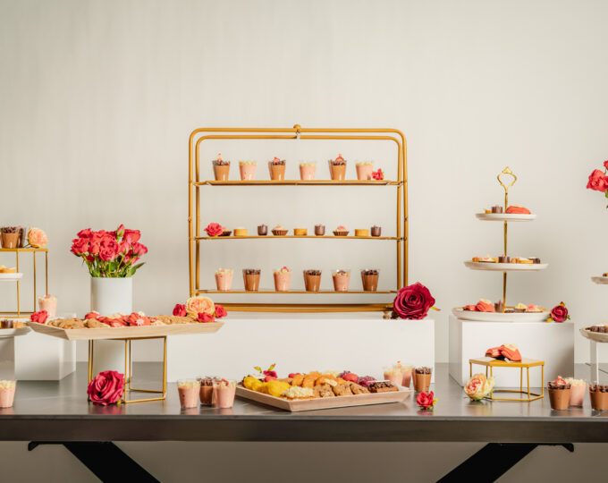 Elegant dessert table by NYC Valentine’s Day catering services with pastries, sweets, and flowers on gold stands.
