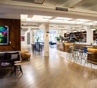Modern open office lounge with a curved café bar, stools, sofas, art on the wall, and wooden floors.