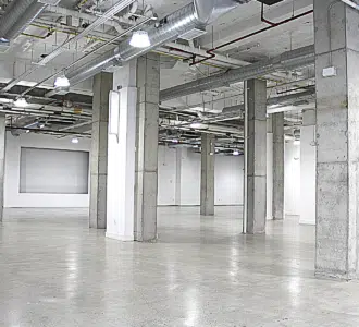 Industrial-style empty room with concrete pillars, white walls, polished floors, and exposed ceiling pipes.