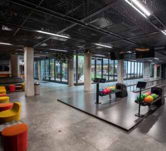 Modern bowling alley with colorful bowling balls, lanes, and vibrant seating in a spacious, open area.