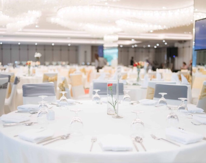 Elegant banquet hall with round tables set for an event, decorated with white linens and single flower centerpieces.