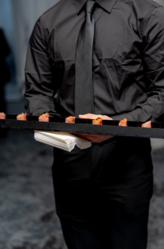 A server in black attire holds a tray of appetizers and napkins at an NYC graduation catering event.