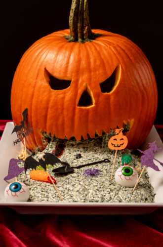 A carved jack-o’-lantern “vomiting” spinach dip decorated with Halloween catering toothpicks and candy eyeballs.
